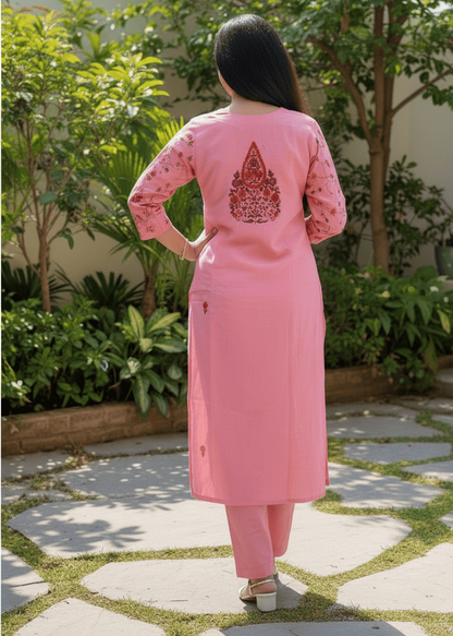 Person wearing a pink outfit with a pattern on the back, standing outdoors on a stone path.