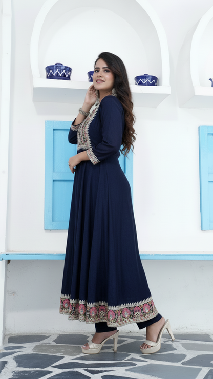 Woman in a navy blue dress with floral patterns standing in front of a white wall with blue accents.