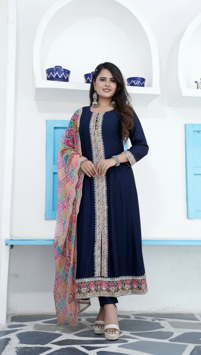 Woman in a navy blue dress with a colorful scarf standing in front of a white wall with blue accents.